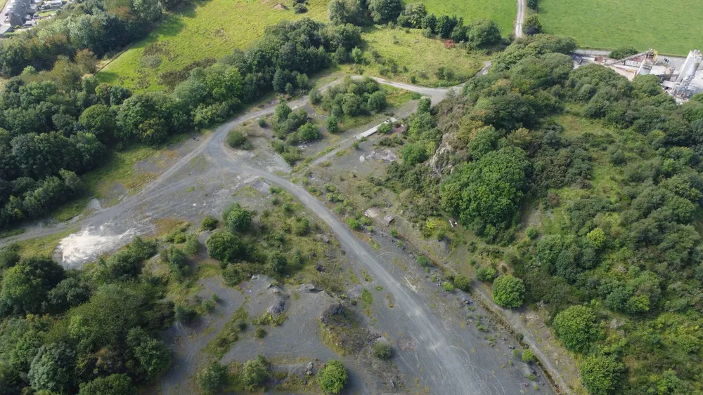 Drone view of a quarry site of bare, disturbed ground with tracks and ponds.