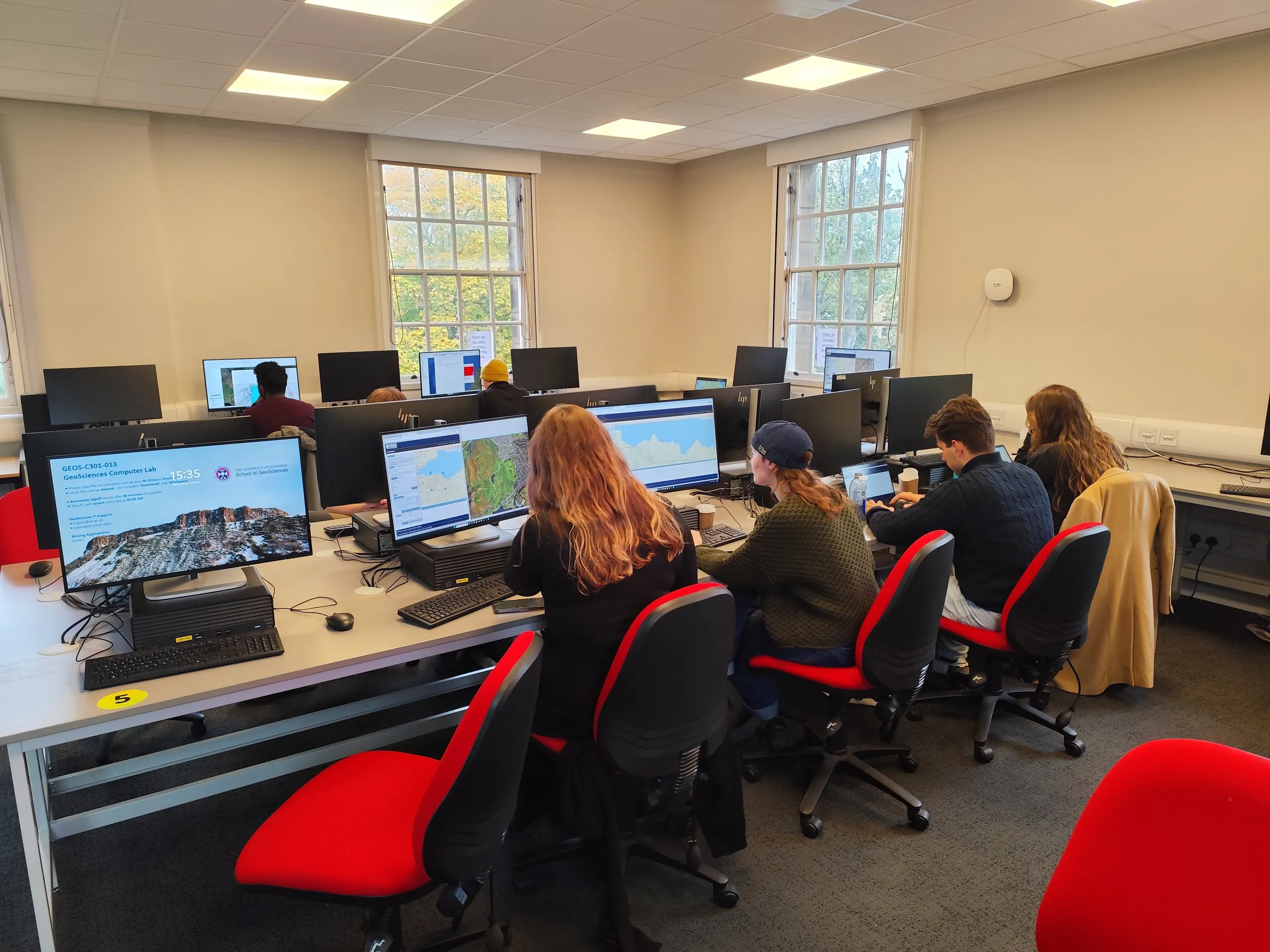 University computer lab with students working at desks, GIS maps on screen.