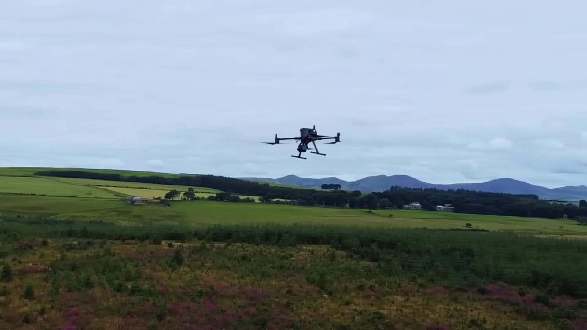 A survey drone flying low over moorland, with hills behind.
