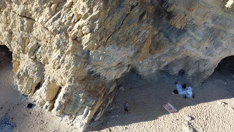 Close drone view of a layered rock face at the foot of a cliff.