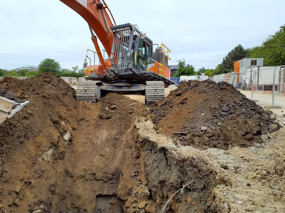 An orange excavator beside a deep trench on a construction site.